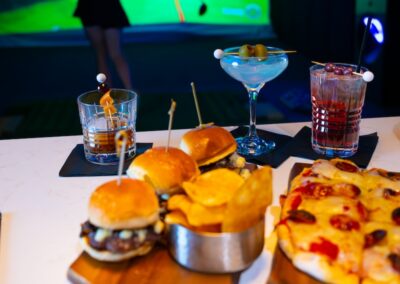 ParT Barn golf simulator bar top with burgers, chips, and pizza along with drinks